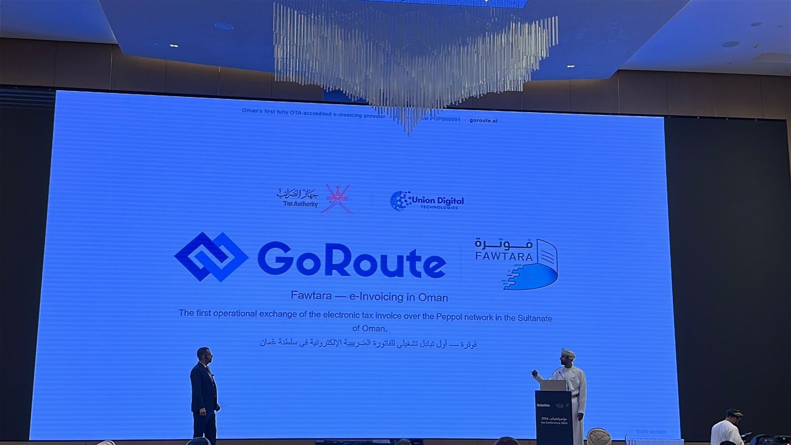 The opening slide at the Oman Tax Conference: GoRoute, Fawtara, the Tax Authority and Union Digital Technologies on screen, Qasim Shah on stage and His Excellency the Chairman at the podium